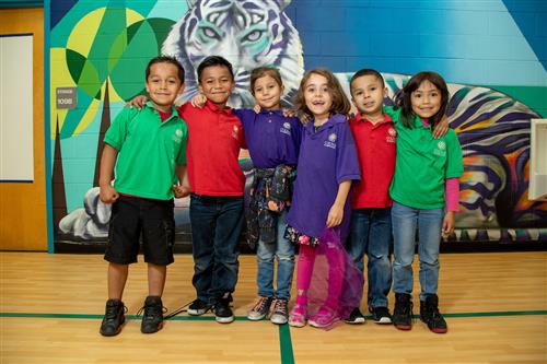 Six elementary students standing arm-in-arm in front of a colorful tiger mural 